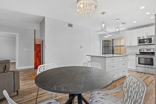 dining space featuring light hardwood / wood-style flooring, a textured ceiling, and a notable chandelier