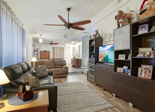 living room with ceiling fan, a textured ceiling, and light wood-type flooring