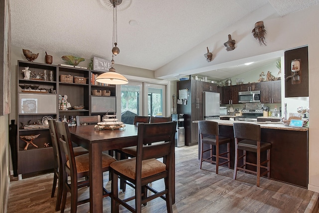 dining area featuring lofted ceiling, a textured ceiling, and hardwood / wood-style floors