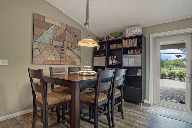 dining room with a textured ceiling, vaulted ceiling, and hardwood / wood-style floors