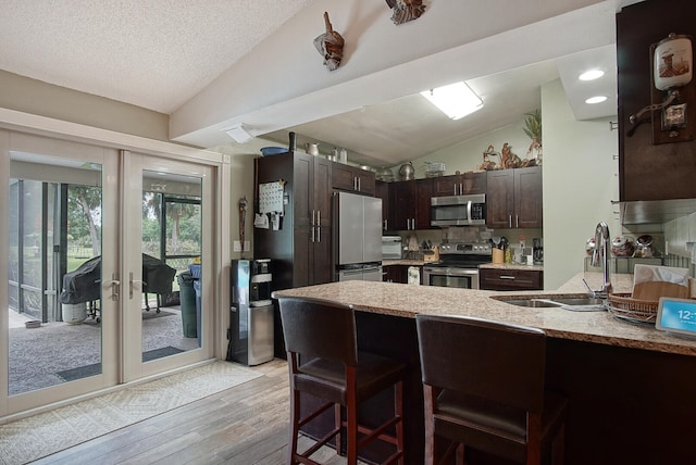 kitchen with light hardwood / wood-style floors, sink, lofted ceiling, kitchen peninsula, and appliances with stainless steel finishes