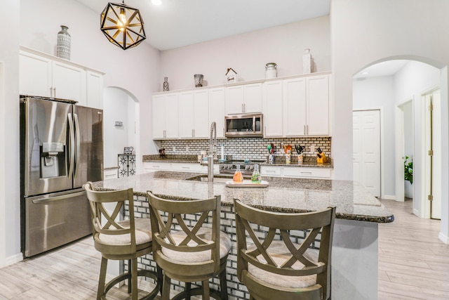 kitchen featuring dark stone counters, white cabinetry, light hardwood / wood-style flooring, stainless steel appliances, and a center island with sink