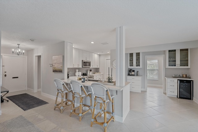 kitchen featuring kitchen peninsula, stainless steel appliances, beverage cooler, a notable chandelier, and white cabinets