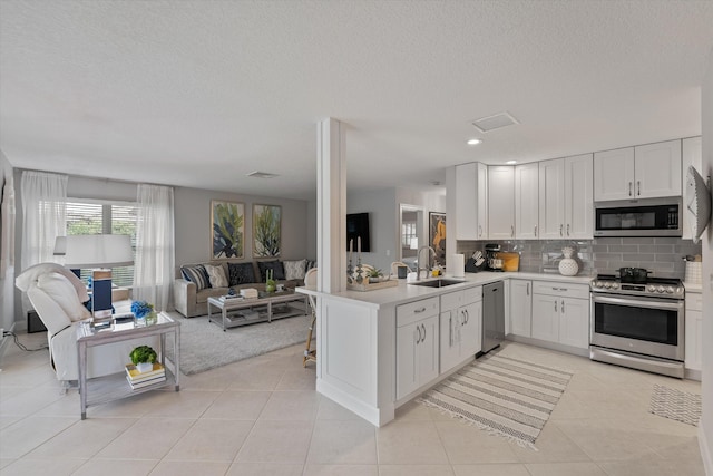 kitchen with kitchen peninsula, stainless steel appliances, sink, white cabinetry, and light tile patterned flooring