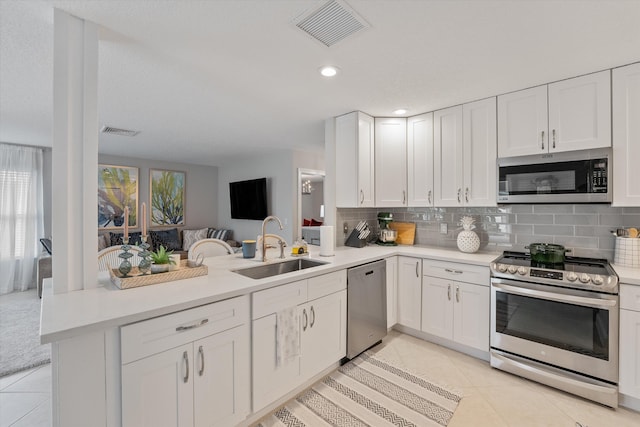 kitchen with sink, light tile patterned floors, kitchen peninsula, white cabinets, and appliances with stainless steel finishes