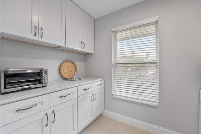 kitchen with white cabinetry, light tile patterned floors, and light stone counters