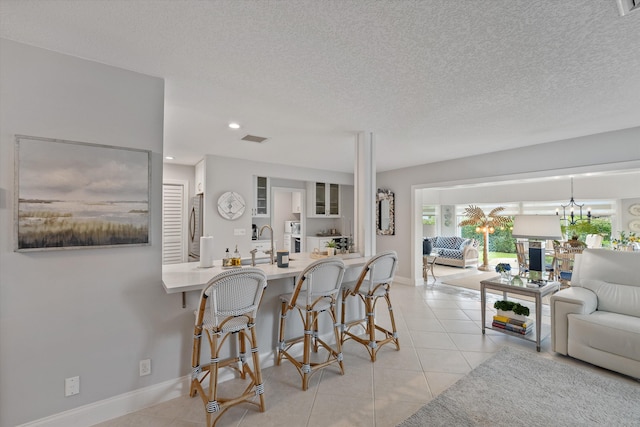 kitchen featuring a kitchen bar, kitchen peninsula, sink, stainless steel refrigerator, and light tile patterned flooring