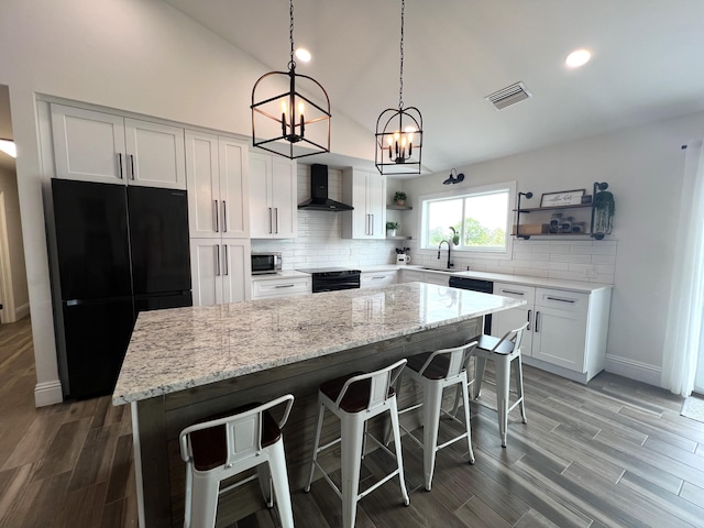 kitchen featuring wood-type flooring, a notable chandelier, a kitchen island, wall chimney range hood, and black appliances