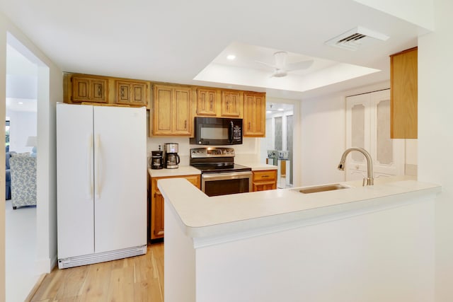 kitchen with white refrigerator, a raised ceiling, kitchen peninsula, stainless steel electric range, and light wood-type flooring