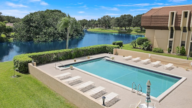 view of swimming pool featuring a lawn, a water view, and a patio