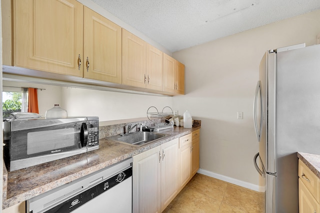 kitchen with a textured ceiling, sink, stainless steel appliances, light tile patterned floors, and light brown cabinetry