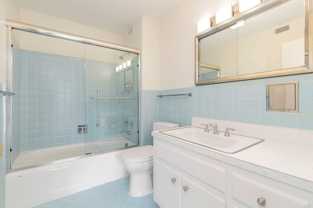 full bathroom featuring toilet, tile walls, tile patterned flooring, shower / bath combination with glass door, and vanity