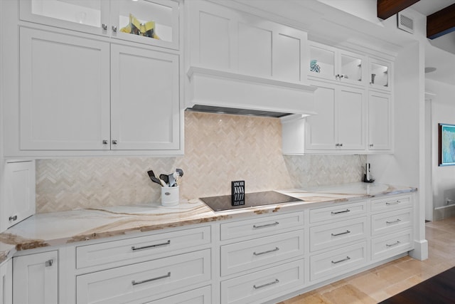 kitchen featuring white cabinets, black electric cooktop, custom range hood, light stone countertops, and decorative backsplash