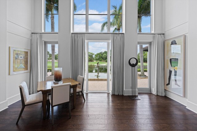 dining area with a towering ceiling, a water view, and dark hardwood / wood-style floors