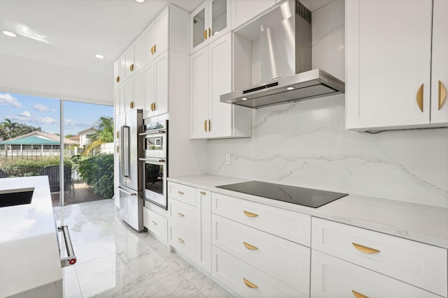 kitchen with appliances with stainless steel finishes, tasteful backsplash, white cabinets, wall chimney exhaust hood, and light stone countertops