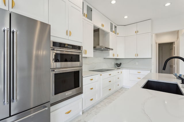 kitchen with light stone counters, white cabinets, stainless steel appliances, sink, and wall chimney range hood