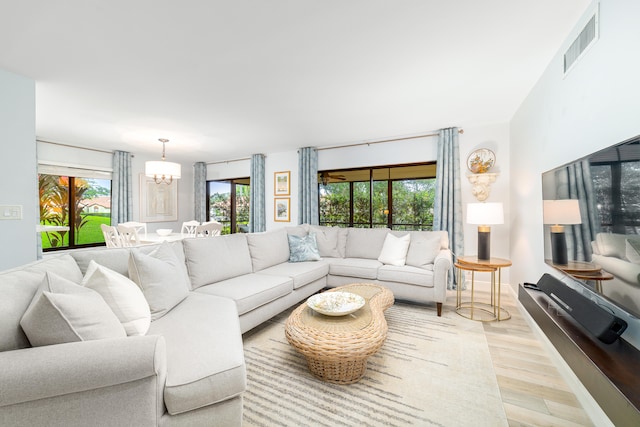 living room with light wood-type flooring, a chandelier, and a wealth of natural light