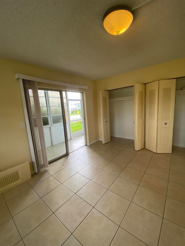 unfurnished bedroom with light tile patterned flooring, access to exterior, and a textured ceiling