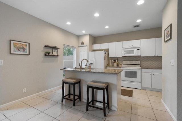 kitchen with decorative backsplash, white appliances, white cabinets, a breakfast bar area, and an island with sink