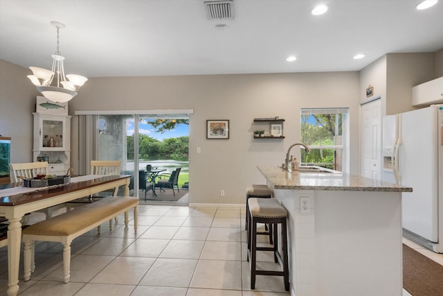 kitchen featuring light stone countertops, sink, white refrigerator with ice dispenser, a notable chandelier, and decorative light fixtures