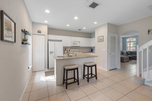 kitchen with a kitchen bar, backsplash, light stone counters, white appliances, and white cabinetry