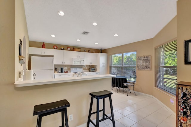 kitchen with white cabinets, light tile patterned floors, kitchen peninsula, white appliances, and a kitchen bar