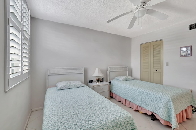 bedroom featuring a textured ceiling, light tile patterned flooring, ceiling fan, and a closet