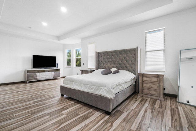 bedroom featuring light hardwood / wood-style flooring, a raised ceiling, and multiple windows