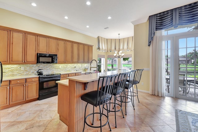 kitchen featuring decorative light fixtures, a center island with sink, backsplash, black appliances, and an inviting chandelier