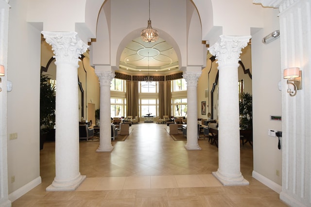 tiled entrance foyer featuring a towering ceiling, a raised ceiling, and ornate columns