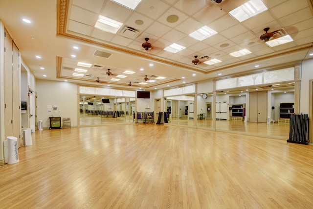 workout area with ceiling fan, light hardwood / wood-style flooring, and a raised ceiling