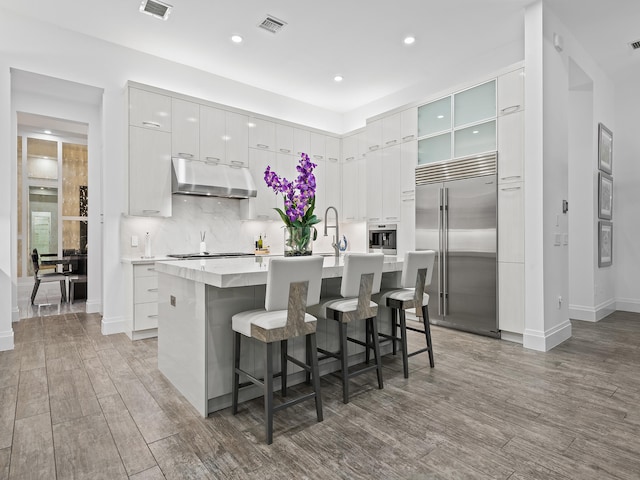 kitchen with a kitchen breakfast bar, white cabinetry, stainless steel appliances, dark hardwood / wood-style floors, and a center island with sink