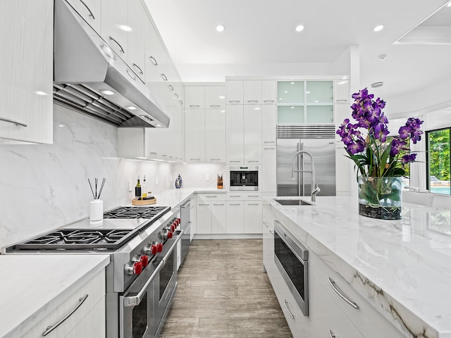 kitchen with built in appliances, backsplash, white cabinetry, light stone counters, and dark hardwood / wood-style flooring