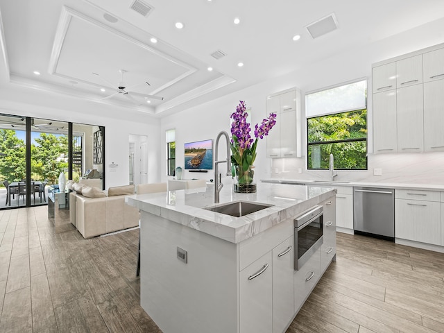 kitchen featuring white cabinets, a raised ceiling, a kitchen island with sink, plenty of natural light, and stainless steel appliances