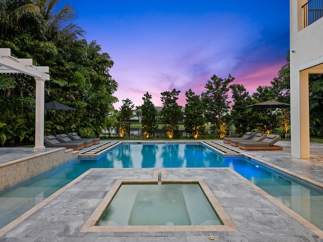 pool at dusk featuring an in ground hot tub and a patio area