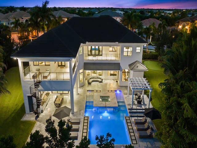 back house at dusk featuring an outdoor hangout area, a pool with hot tub, a balcony, an outdoor bar, and a patio