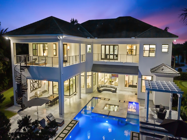 back house at dusk featuring a patio area, a pool with hot tub, and an outdoor hangout area