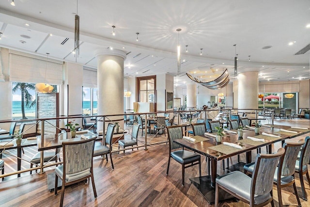 dining space featuring a water view, hardwood / wood-style floors, and ornate columns