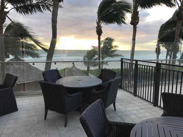 patio terrace at dusk with a balcony, a water view, and a beach view