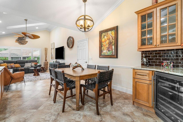 dining space featuring wine cooler, bar area, lofted ceiling, ceiling fan with notable chandelier, and ornamental molding