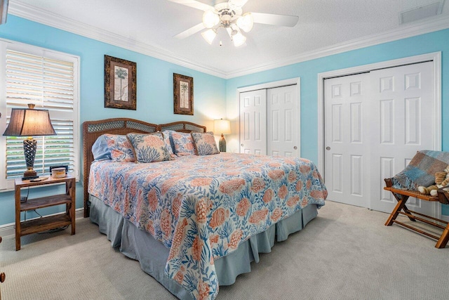 carpeted bedroom featuring ceiling fan, ornamental molding, a textured ceiling, and multiple closets