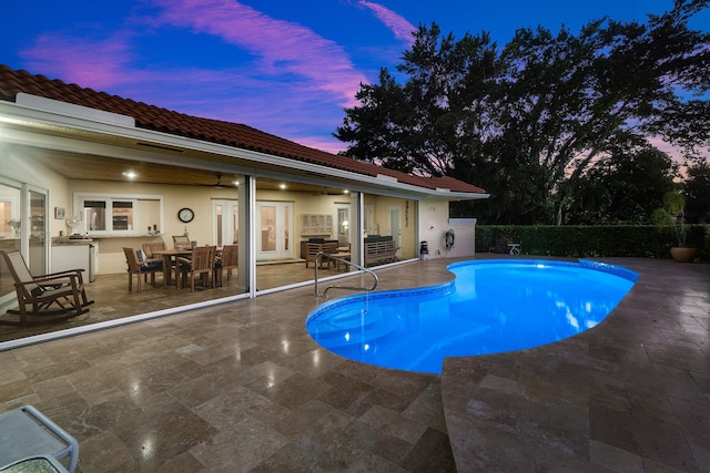 pool at dusk with ceiling fan and a patio