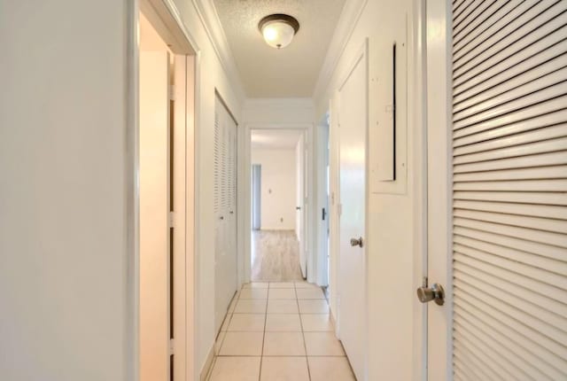 corridor with a textured ceiling, ornamental molding, and light tile patterned flooring