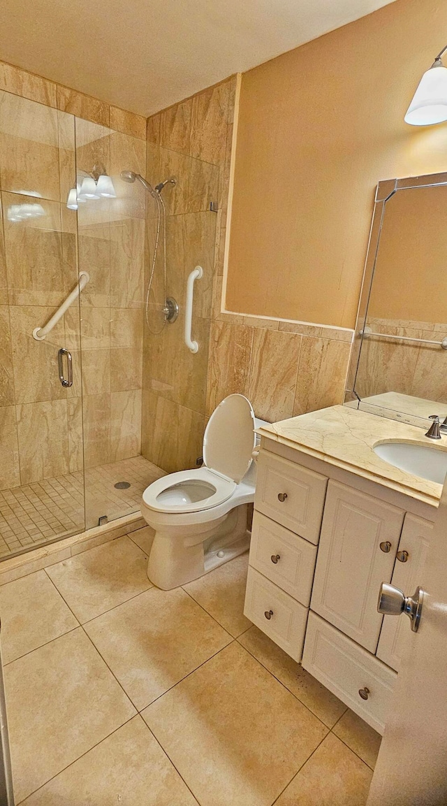 bathroom with a shower with door, tile patterned floors, tile walls, toilet, and vanity