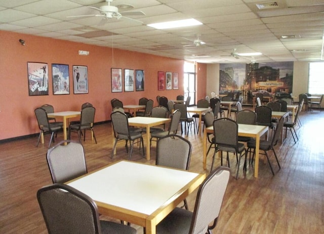 dining space with ceiling fan, a drop ceiling, and hardwood / wood-style floors