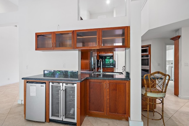 kitchen with a towering ceiling, beverage cooler, light tile patterned floors, and sink