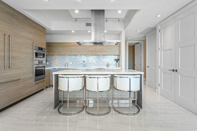 kitchen featuring a large island, decorative backsplash, a raised ceiling, and a kitchen bar