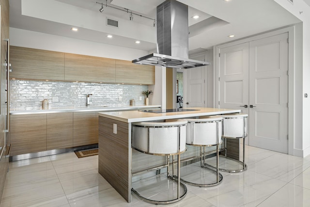 kitchen with an island with sink, island exhaust hood, backsplash, a kitchen breakfast bar, and black electric stovetop