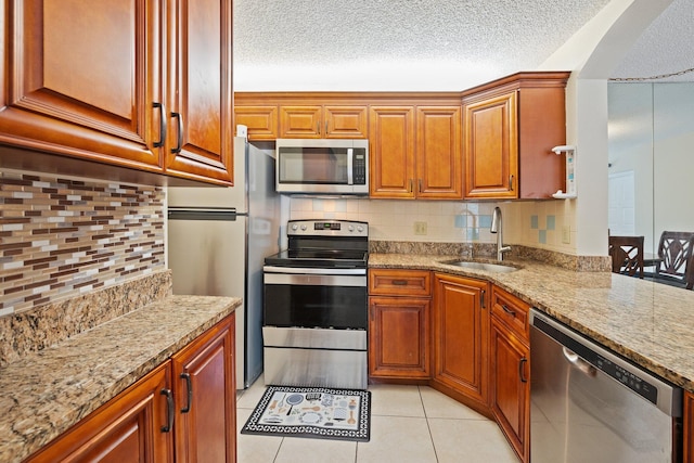 kitchen featuring light stone countertops, backsplash, stainless steel appliances, sink, and light tile patterned floors