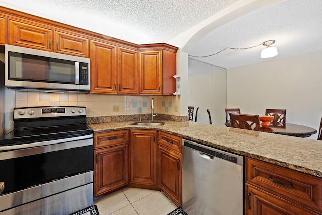 kitchen featuring sink, decorative backsplash, a textured ceiling, light stone counters, and stainless steel appliances